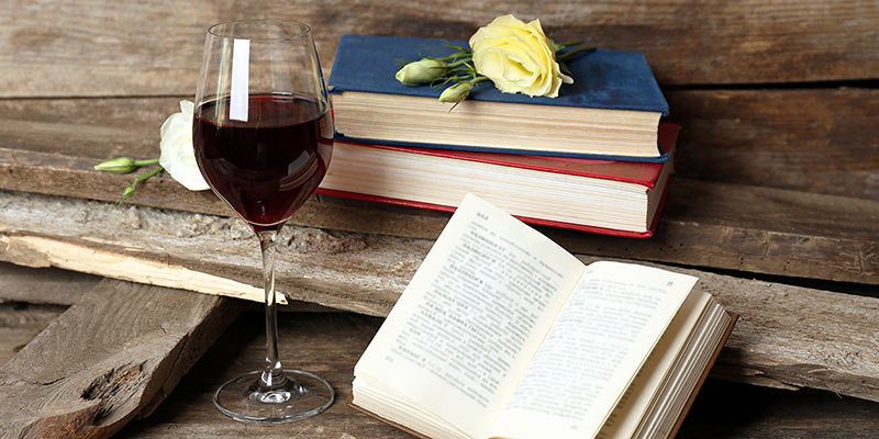 Ein Glas Rotwein steht zusammen mit Büchern auf einem Tisch