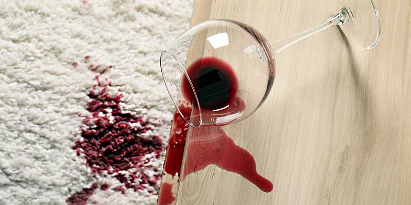 Umgekipptes Weinglas hat Rotwein auf weißen Teppich verschüttet