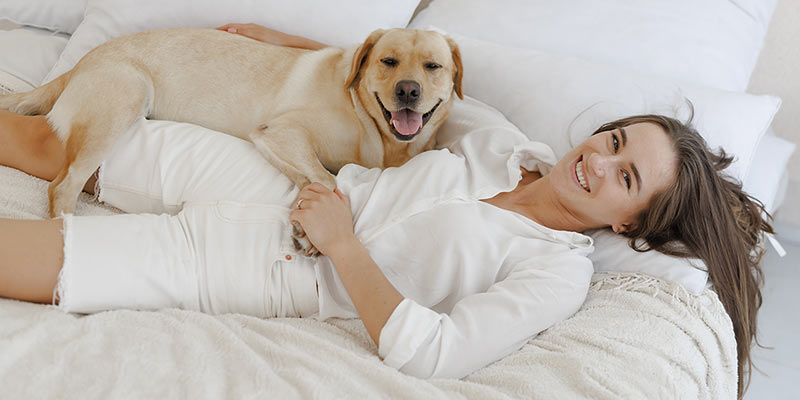 Frau und Hund liegen glücklich auf einem Bett