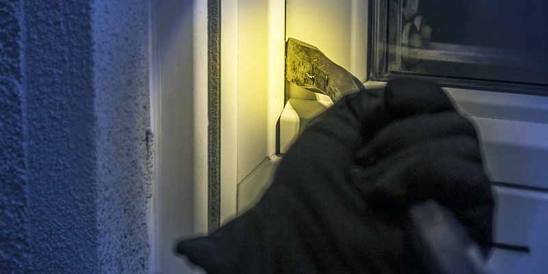 Ein Einbrecher versucht durch ein Fenster in eine Wohnung zu gelangen