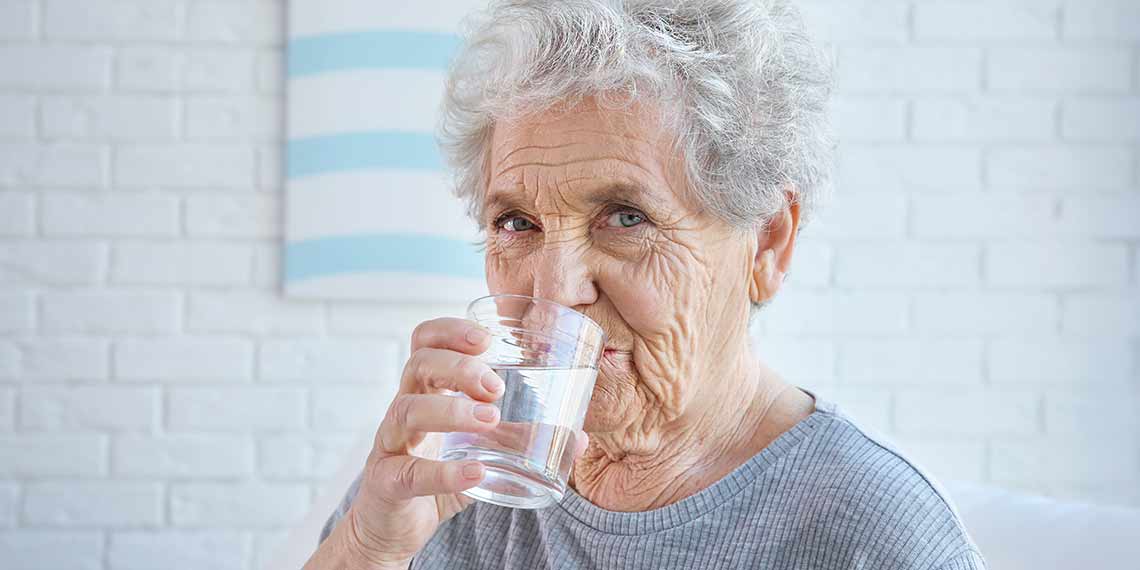 Eine Seniorin trinkt Wasser aus einem Glas