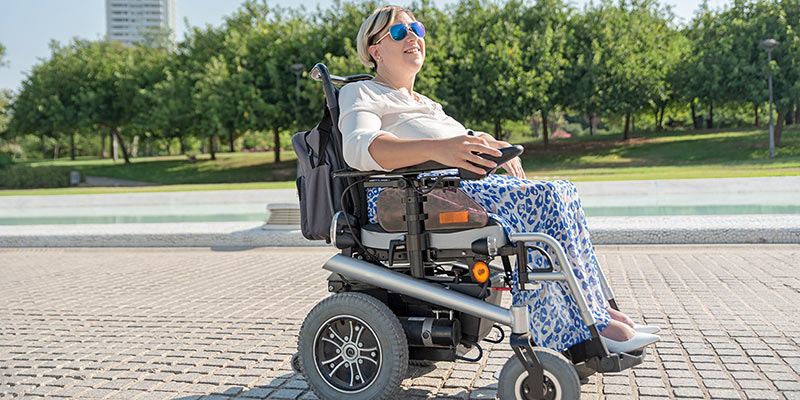 Frau fährt an einem sonnigen Tag mit ihrem elektrischen Rollstuhl