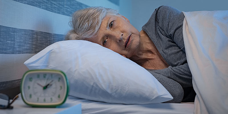 Ältere Frau liegt im Bett und leidet an Schlaflosigkeit
