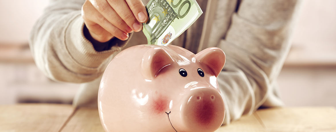 Ein Mensch steckt 100 Euro in ein Sparschwein