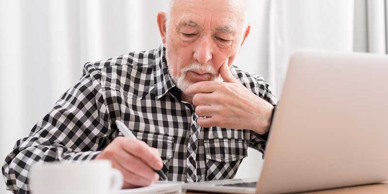 Älterer Herr macht sich Notizen am Laptop.