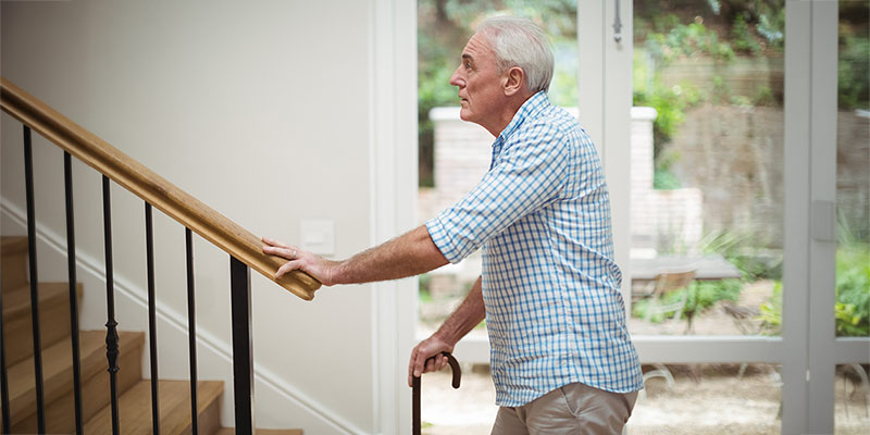 Senior mit Gehstock steht vor einer Treppe