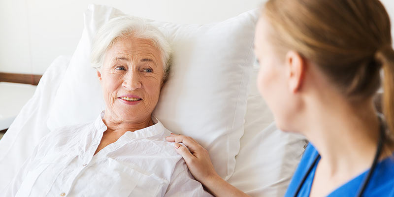 Bettlägerige Seniorin wird von Pflegerin begutachtet.