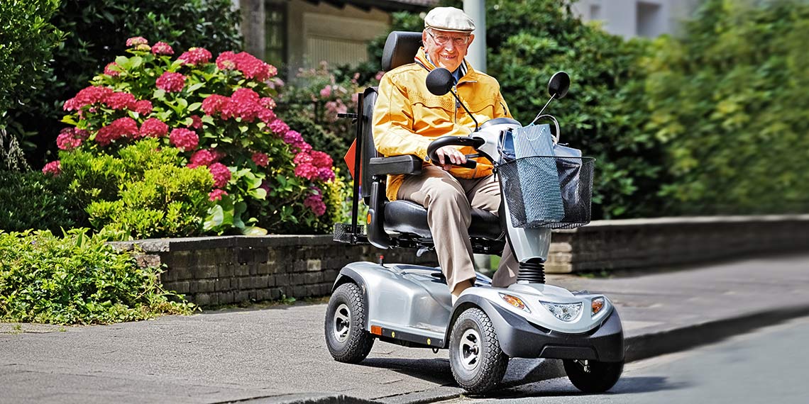 Senior sitzt in seinem Elektromobil und fährt draußen auf dem Bürgersteig