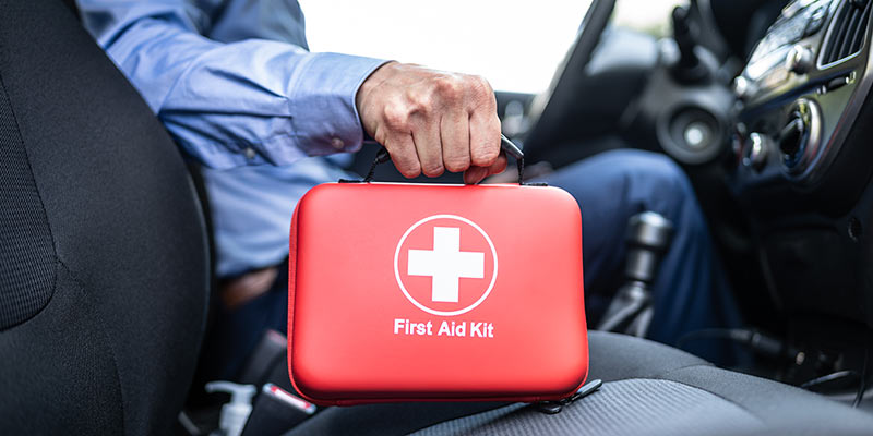 Ein Mann hält in seinem Auto einen roten Erste-Hilfe-Kasten in der Hand