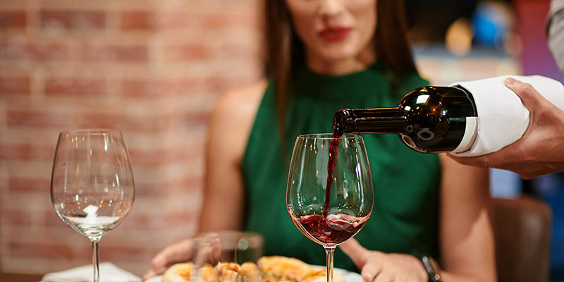 Kellner füllt Weinglas von einer Frau