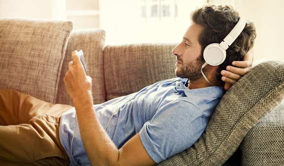 Mann liegt entspannt mit einem Smartphone in der Hand auf einem Sofa