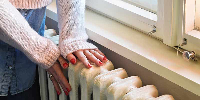 Frau hält ihre Hände an eine Heizung um sich zu wärmen