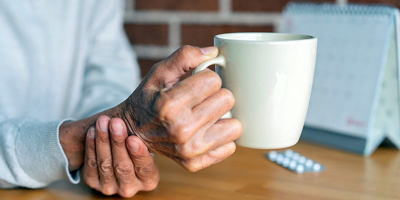 Ältere Frau mit Parkinson stützt ihre zitternde Hand beim Halten einer Tasse