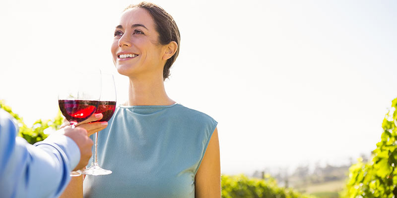 Lächelnde Frau stößt mit Rotwein auf einem Weinberg an