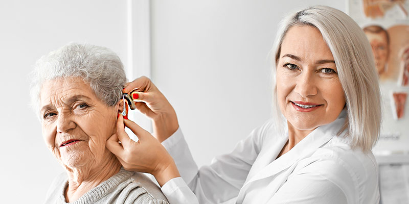 Eine Ärztin setzt einer älteren Frau im Krankenhaus ein Hörgerät ins Ohr