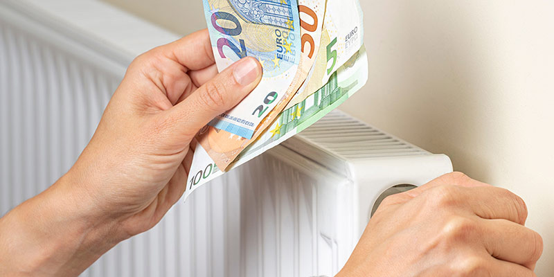 Eine Person mit Geldscheinen in der Hand regelt die Temperatur am Heizkörper