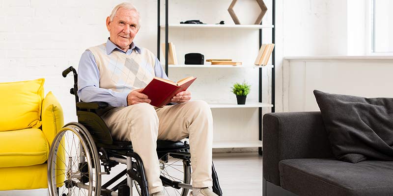 Älterer Mann sitzt in einem Rollstuhl und liest ein Buch