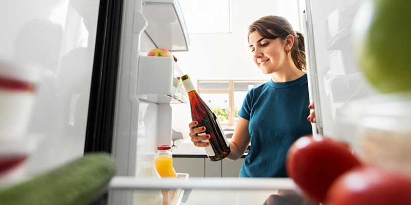 Eine junge Frau holt eine Flasche Wein aus einem Kühlschrank